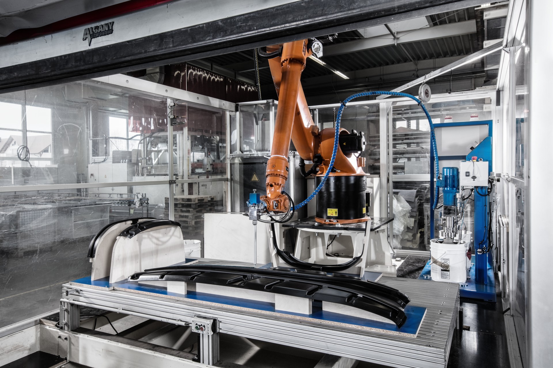 Oranger ROboterarm bearbietet ein schwarzes Plastikteil in einer swissplast Fabrik