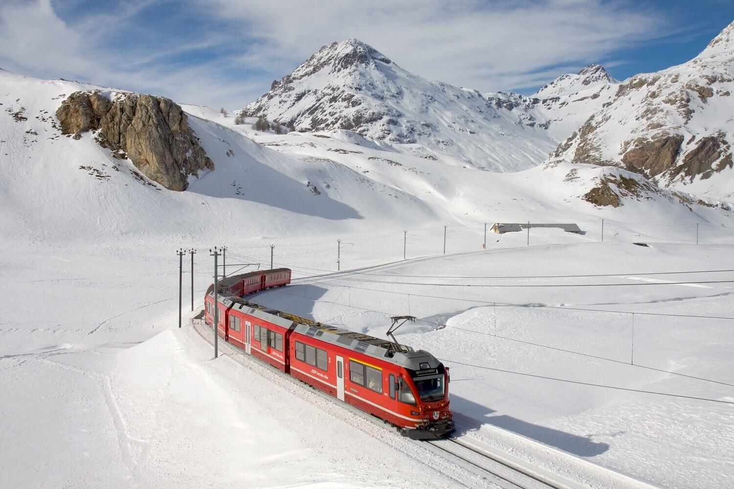 Elektrische Bahn fährt durch Schweizer Schneelandschaft mit Bergen im Hintergrund