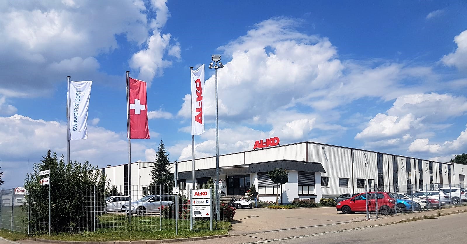 Das AL-KO Gebäude an einem schönen Tag mit swissplast Flagge, Schweizer Flagge und AL-KO Flagge