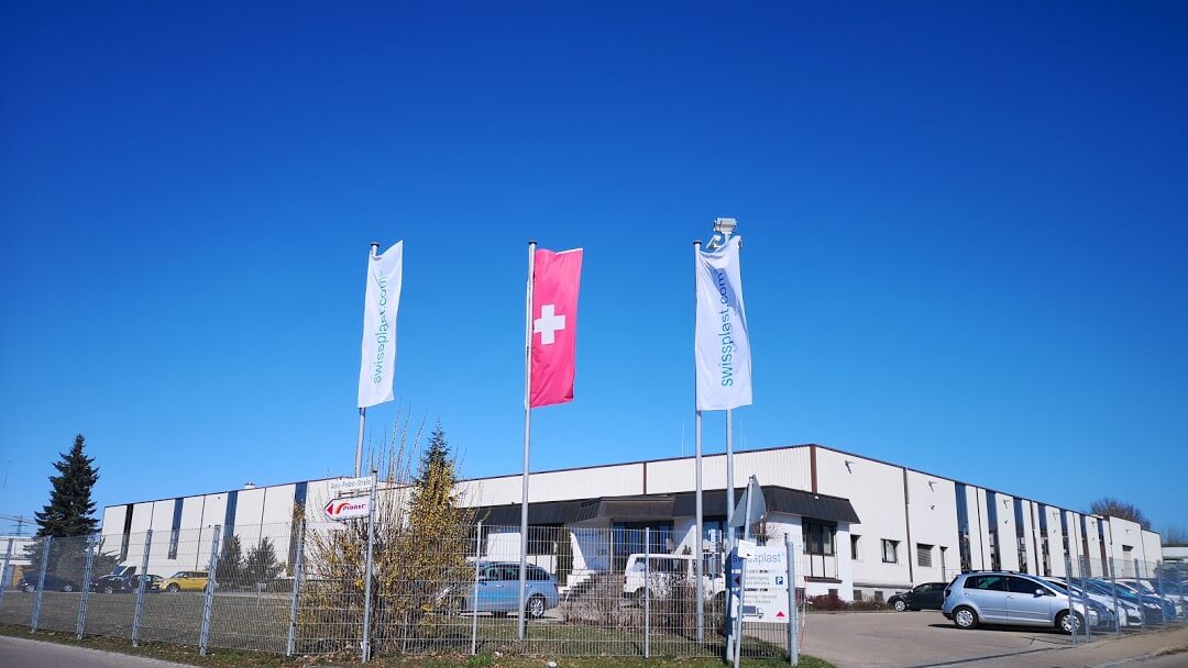 Zwei swissplast Flaggen und eine Schweizer Flagge stehen vor dem swissplast Firmengebäude